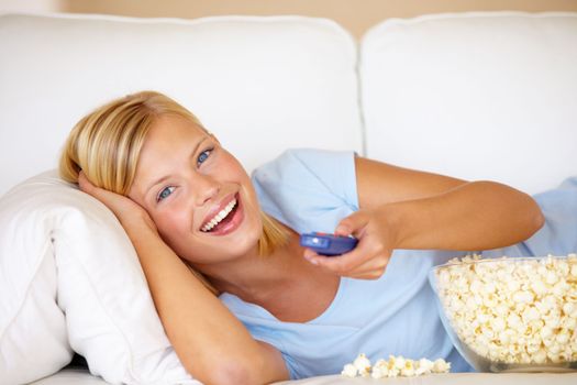 Its movie night. Young woman lying on the couch and watching tv while eating popcorn.