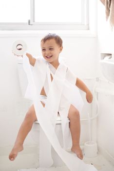 Potty training can be a challenge...Humorous shot of a young boy sitting on a toilet wrapped in toilet paper.