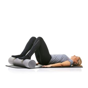 Using a foam-roller to raise her legs. A young woman lying on an exercise mat with her feet on a foam roller.