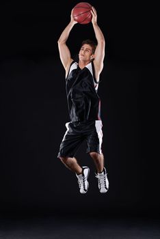 Going for a slam dunk. Full length studio shot of a young male basketball player in action against a black background.