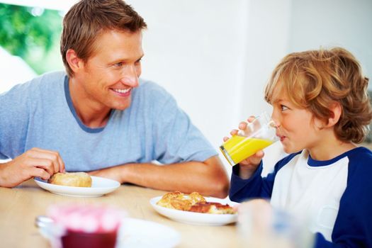 Father and son having breakfast while looking at each other. Portrait of a happy father and son having breakfast while looking at each other.
