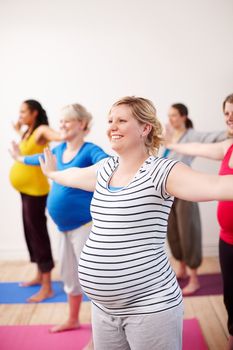 Preparing our bodies for the challenges of motherhood. A multi-ethnic group of pregnant women doing exercises with their arms stretched to the side.