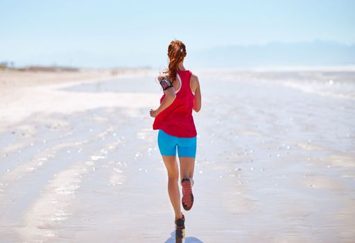 Getting her fitness on at the beach. Rearview shot of a young woman running on the beach.
