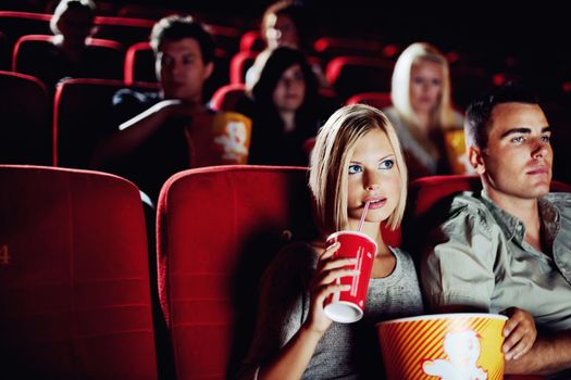 Engrossed in a great movie. A beautiful woman drinking a refreshment and eating popcorn with her boyfriend at the movies - Copyspace.
