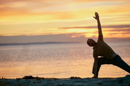 Stretch the body, stretch the mind. a man practicing the triangle pose during his yoga routine at the beach.