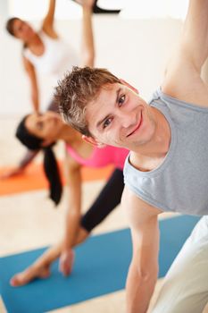 Putting some macho into yoga. A young man smiling at the camera while doing a stretch in yoga class.