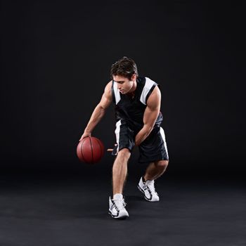 He plays to win. Full length shot of a male basketball player in action against a black background.