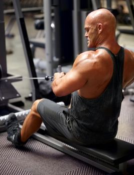 Building up his bulging muscles. Rearview shot of a male bodybuilder using an exercise machine at the gym.