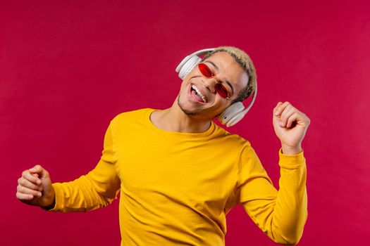 Positive american man listening music, enjoying dance with headphones on red studio background. Radio, wireless modern sound technology, online player.