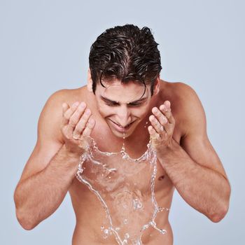 Getting in a deep cleanse. Studio shot of a bare-chested young man splashing water on his face.