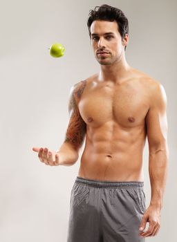 Healthy and fit. Portrait of a macho young man throwing an apple in the air.