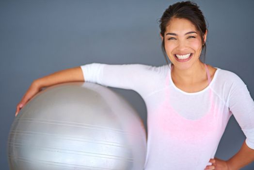 Cmon, its fun. a sporty young woman holding a pilates ball against a grey background.