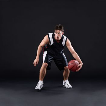 Dribbling pro. Full length shot of a male basketball player in action against a black background.