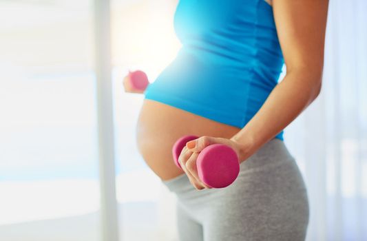 Staying strong through her pregnancy. a pregnant woman working out with weights at home.