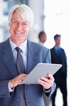 Senior male executive using tablet PC. Portrait of senior male executive using tablet PC with executives in background.