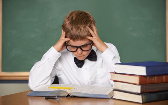 Struggling with the workload...An overwhelmed schoolboy in a bow-tie and glasses sitting with his hands in his hair.