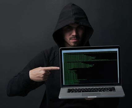 How secure is your laptop really. Portrait of an unidentifiable computer hacker holding up a laptop against a dark background.