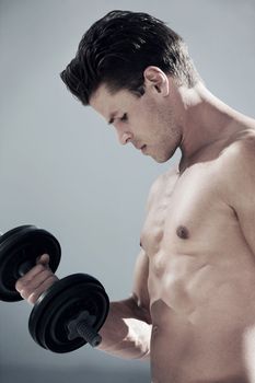 Feeling the burn...A side view of a muscular male lifting weights and looking at his biceps.