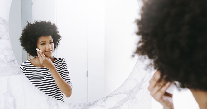Starting her day by glowing. a confident young woman wiping her face with a cleanser while looking into a mirror in the bathroom at home during the day.