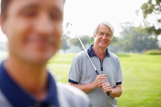 Senior man holding a golf club and smiling. Portrait of senior man holding a golf club and smiling with son in foreground.