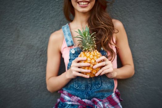 Did anybody ask for a pineapple. an unrecognizable young woman holding a pineapple while standing against a grey background.