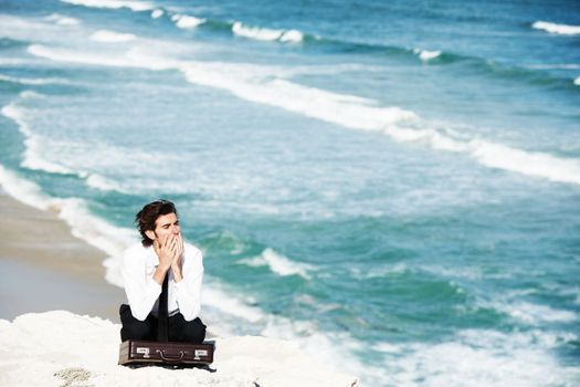 Taking in the majesty of nature. Young businessman sitting on a cliff above the ocean with his briefcase.