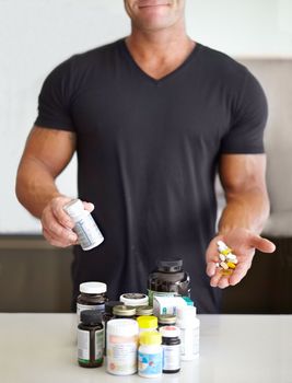Getting some outside help to build mass. Cropped image of a muscular man holding a handful of pills and holding a pill bottle.