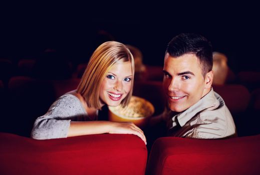 Cosy at the cinema. A cute young couple smiling while on a date at the cinema.