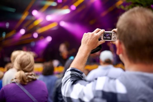Living life at shutter speed. Rearview shot of a man in the crowd holding a camera to photograph a concert.
