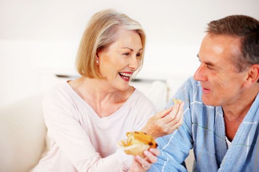 Cheerful mature woman feeding muffin to her husband. Portrait of a cheerful mature woman feeding muffin to her husband.