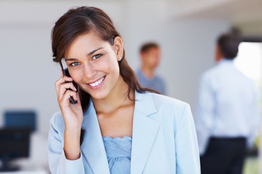 Attractive business woman talking on cellphone. Closeup of young attractive business woman smiling on call with business people in background.