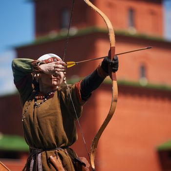 Medieval archery tournament. A woman shoots an arrow in the medieval castle yard. Woman in medieval dress with a wooden bow in her hands. historical reconstruction. 14.05,2022. Yoshkar-Ola, Russia