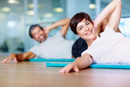 Woman exercising in fitness center. Beautiful woman exercising on yoga mat with man in background.