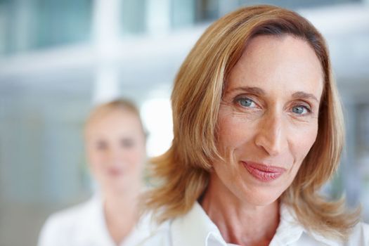 Mature female executive with business woman. Closeup of pretty mature business woman smiling with female executive in background.