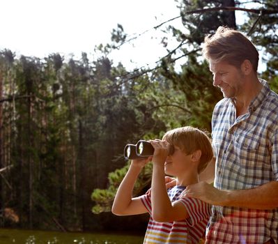 Showing him the beauty of nature. a young boy looking through binoculars while with his father in the outdoors
