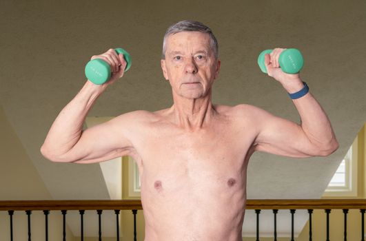Senior man shirtless and exercising in bedroom with dumbbell