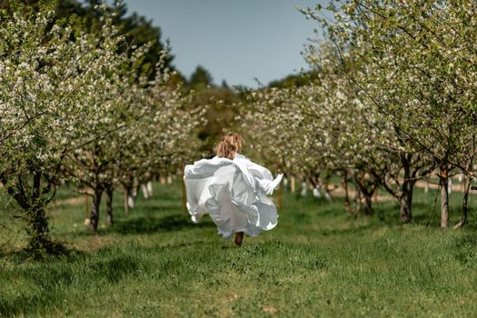 A woman in a white dress runs through a blossoming cherry orchard. The long dress flies to the sides, the bride runs rejoicing in life.