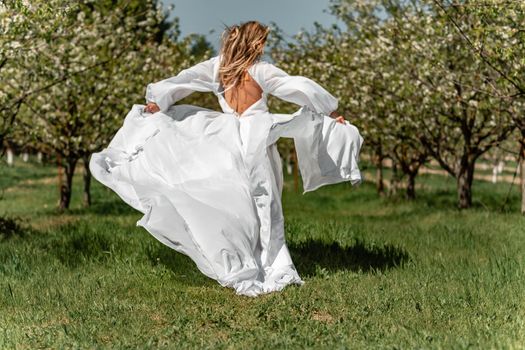 A woman in a white dress runs through a blossoming cherry orchard. The long dress flies to the sides, the bride runs rejoicing in life.
