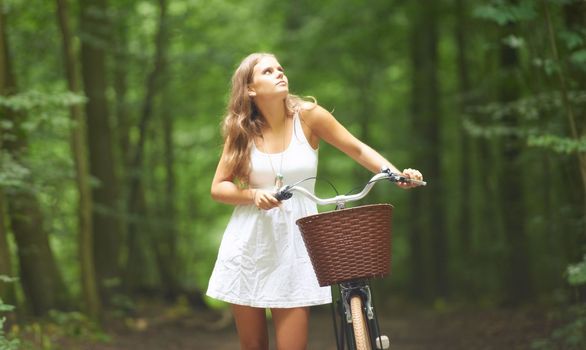 She is the picture of innocence. A pretty young woman walking in the forest with her bicycle.