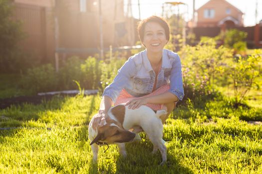 Young woman plays with her dog on the grass on backyard. The concept of animals and friendship or pet owner and love