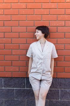 Cheerful woman in home wear pajama outdoor brick wall background emotions - sleepwear and homewear