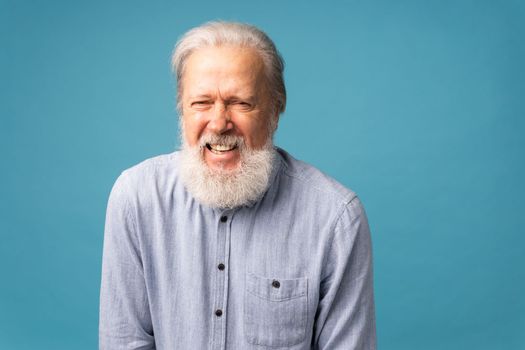 Retired old man with white hair and beard laughter excited over blue color background
