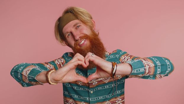 Smiling redhead man makes heart gesture demonstrates love sign expresses good feelings and sympathy