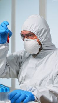 Scientist in sterile chemistry suit analysing blood sample from test tub