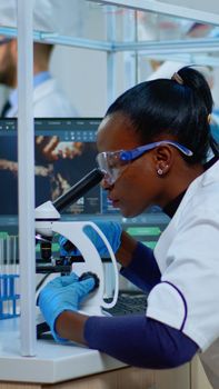 Black woman chemist analysing reaction of virus on microscope