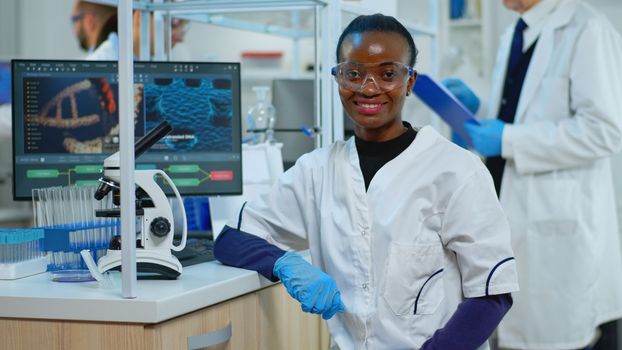 Black doctor woman smiling at camera sitting in scientific lab