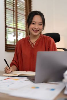 Asian Business woman writing saving account balance with working at home, account and saving concept