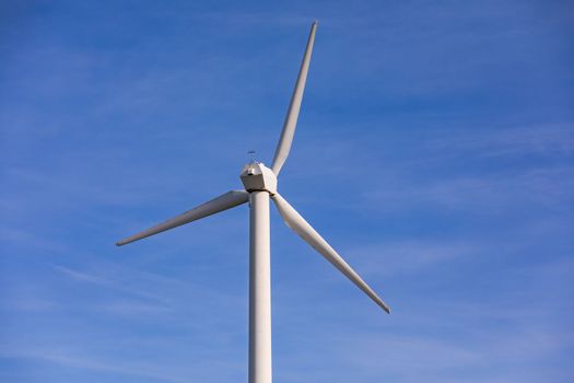 A white wind turbine with three propellers against the blue sky