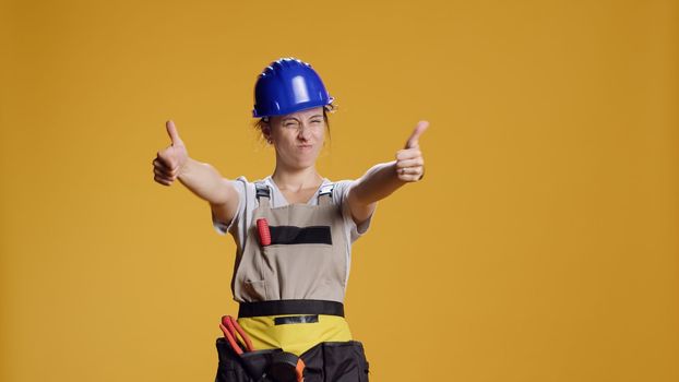 Portrait of female construction worker giving thumbs up in studio