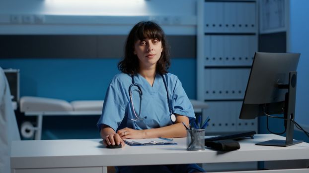 General practitioner nurse sitting at desk working over hours at patient diagnosis report